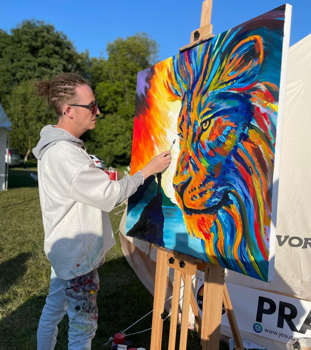 Dave painting a lion using many vibrant colours whilst outside